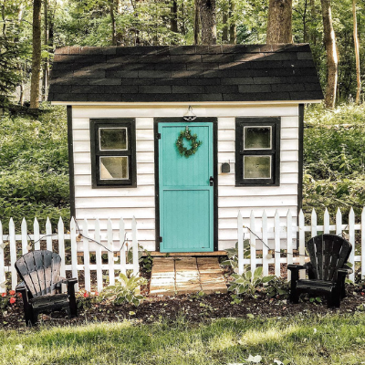 little white house with blue door and picket fence in the woods